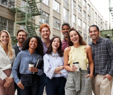 Friendly coworkers laugh to camera outside their workplace